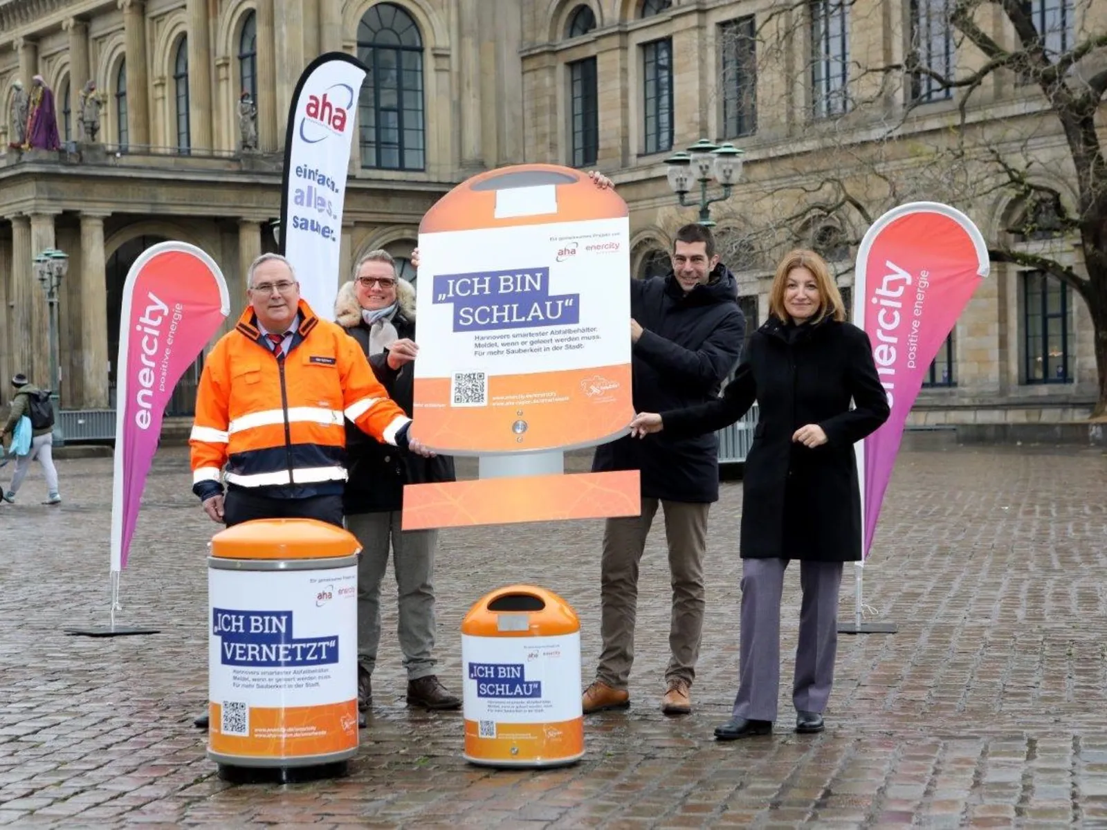 Drei Männer und eine Frau stehen vor dem Neuen Rathaus in Hannover und halten ein Werbeschild mit der Aufschrift Ich bin schlau.