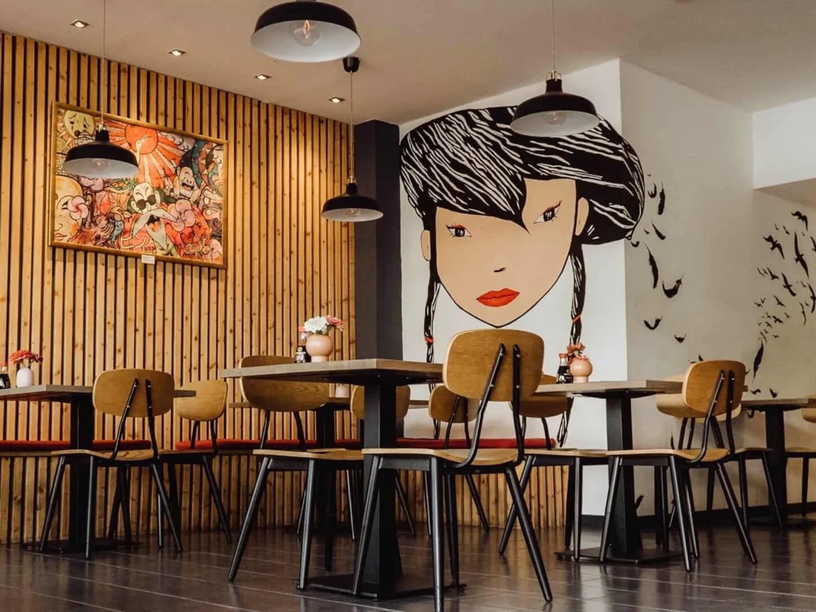 Interno di un ristorante asiatico con pareti in legno, tavoli e sedie, oltre a un grande murale raffigurante una donna dai capelli neri.