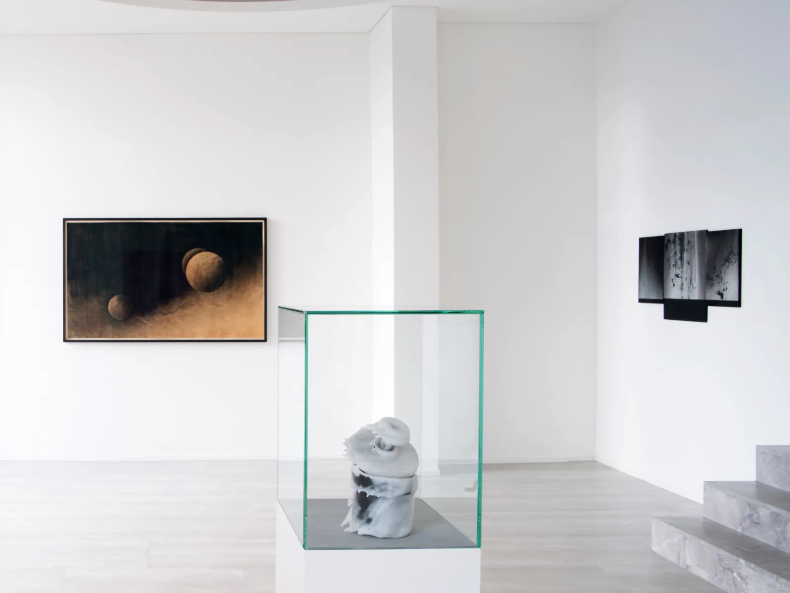 Moderni galleria, jossa on lasivitriinissä oleva veistos ja kaksi abstraktia seinämaalausta valkoisella taustalla.