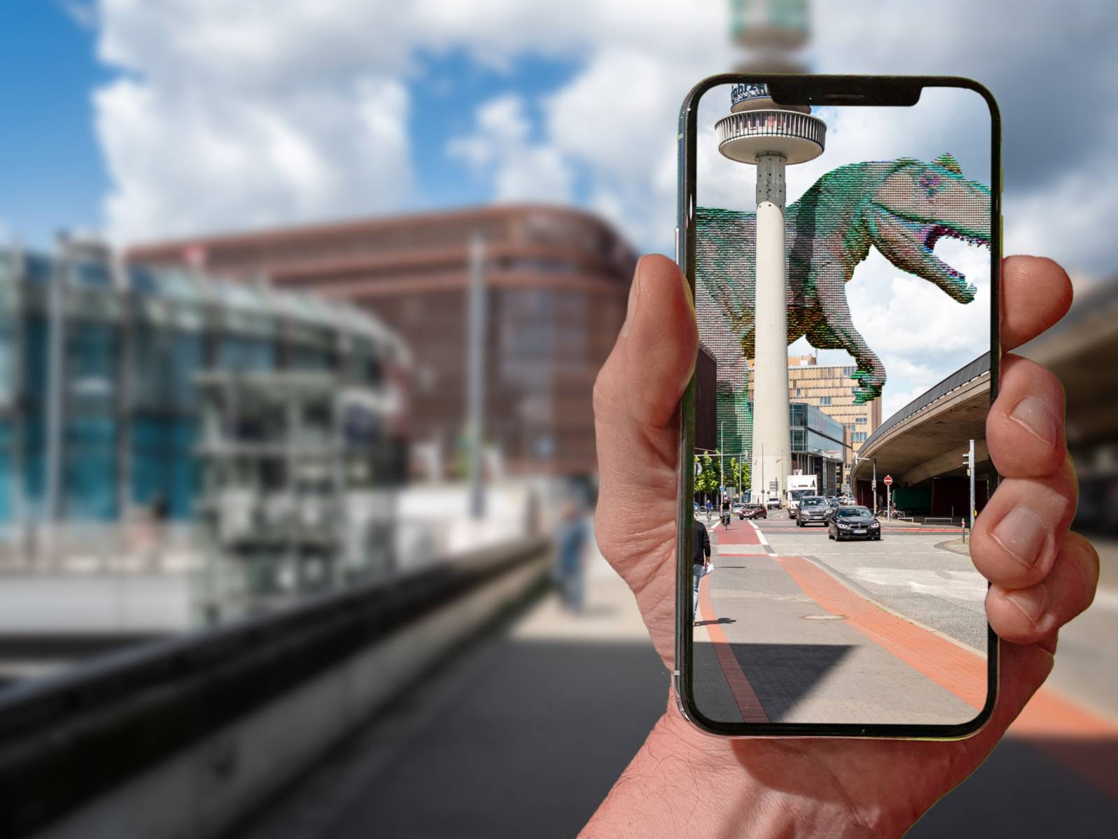 En gade i Hannover. Foran den holder en hånd en mobiltelefon. På skærmen vises en dinosaur på gaden.