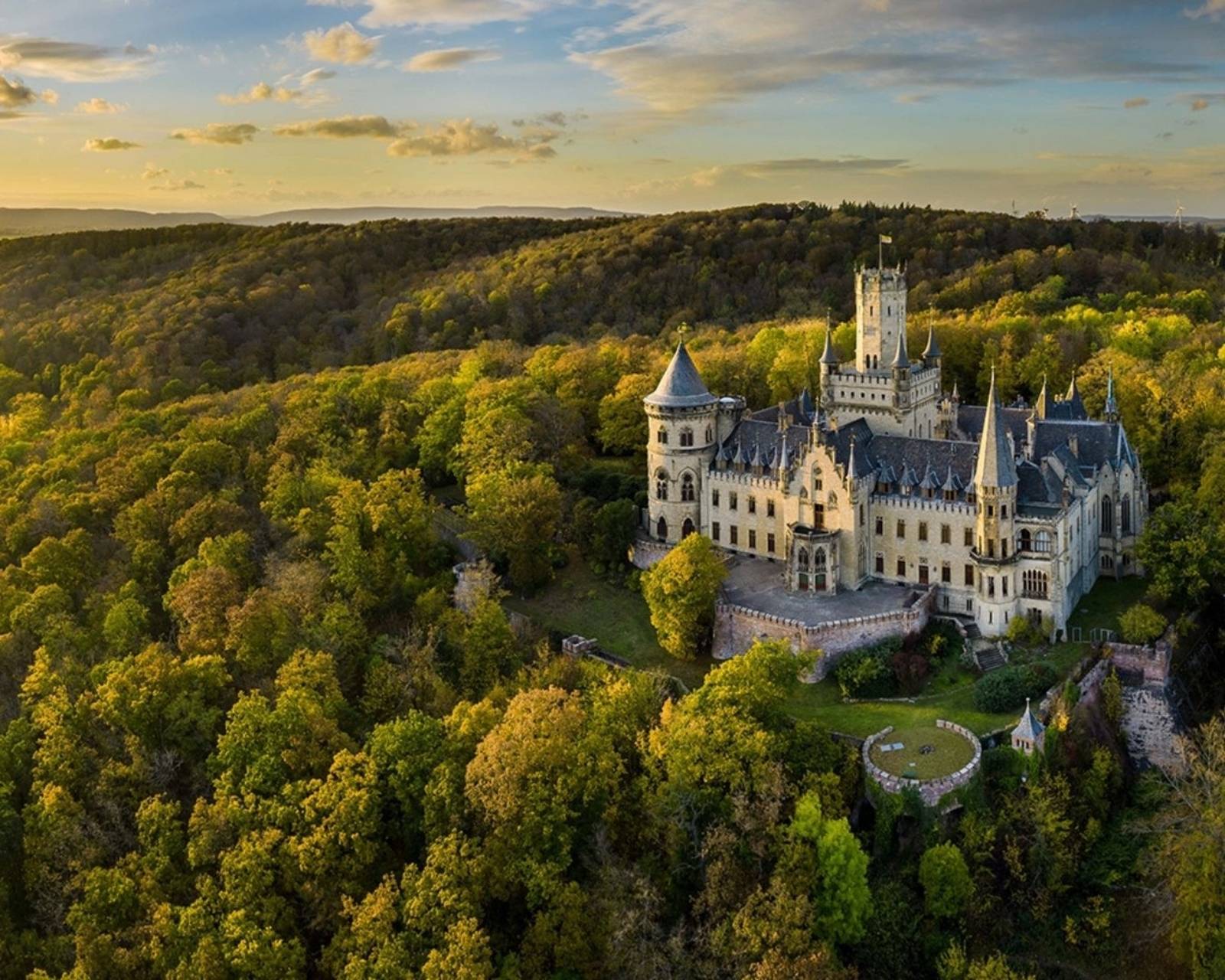 Schloss Marienburg im Abendlicht, umgeben von herbstlichem Wald und Flusslandschaft in Niedersachsen.