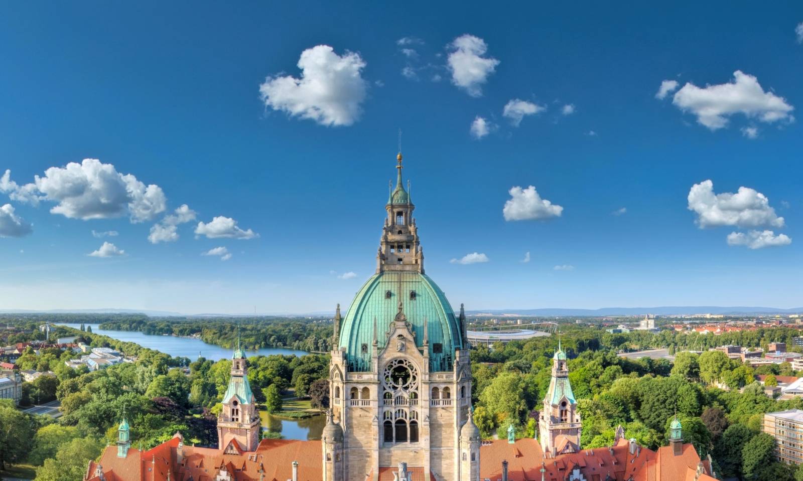Rathaus Hannover mit grüner Kuppel, umgeben von Parkanlagen und Maschsee unter blauem Himmel.