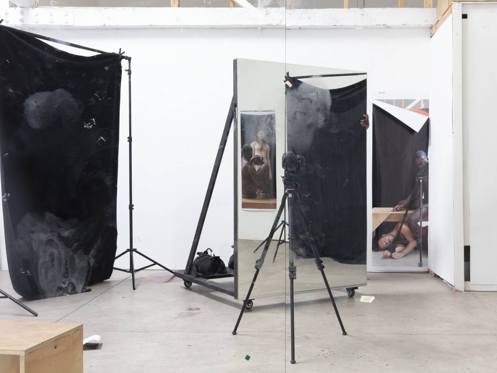 Zu sehen ist eine Fotografie von Paul Mpagi Sepuya. Sie zeigt eine Fotostudio mit Abblendwand, Spielen und Stativ.