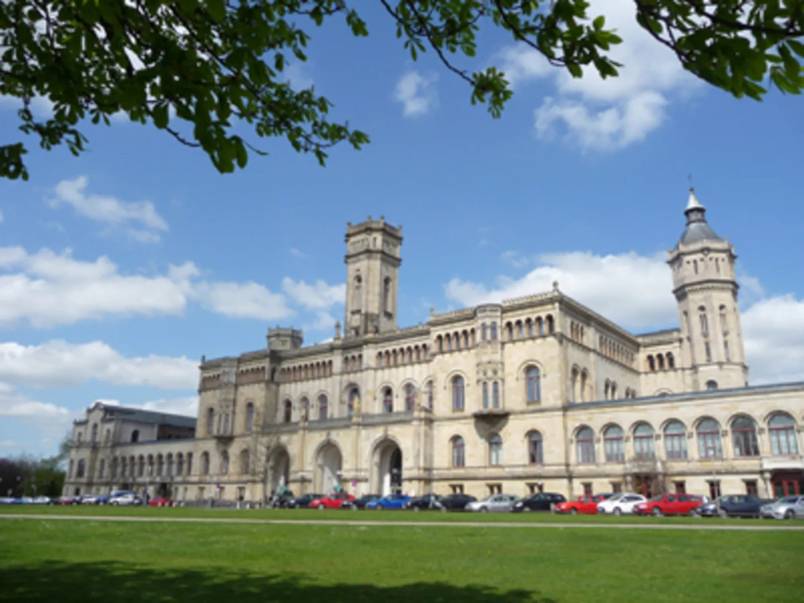 Vor einem schlossähnlichen Gebäude parken mehrere Autos.