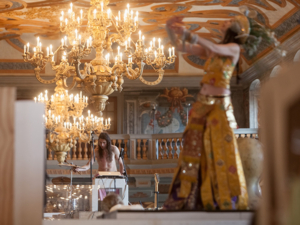 A dancer in the foreground, in the background a musician standing below the chandeliers in the gallery building in Herrenhausen