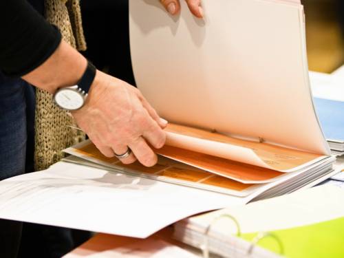 Eine ältere Person blättert durch einen Aktenordner und sichtet Unterlagen.