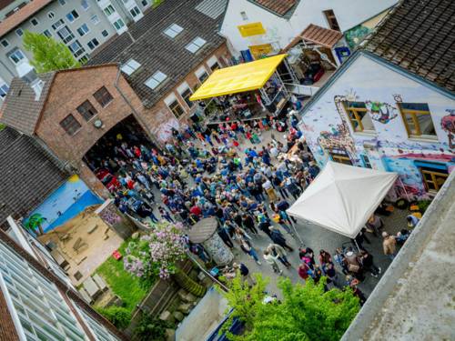 Der Innenhof einer alten Bettfedernfabrik im Mai mit zahlreichen Menschen, die eine Fete feiern.