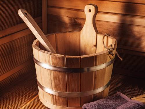Saunaeimer aus Holz mit Holzlöffel und Handtuch auf einer Saunabank