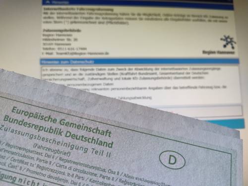 Fahrzeugbrief vor einer Anmeldemaske auf einem Bildschirm