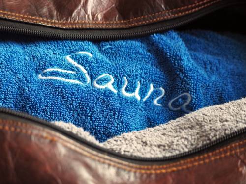Blick in eine geöffnete Sporttasche auf ein Handtuch mit einer Stickerei. Auf dem Handtuch steht gut sichtbar gestickt: Sauna