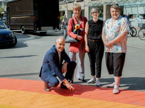 Vier Personen an einem Regenbogen, der gerade auf den Asphalt gespr&uuml;ht wird.