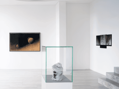 Moderne Galerie mit Skulptur in Glaskasten und zwei abstrakten Wandbildern auf weißem Hintergrund.