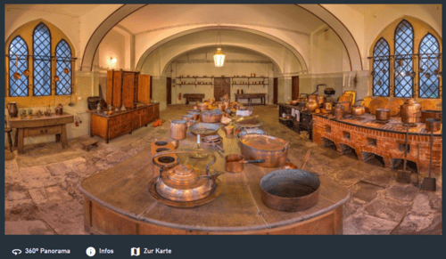 Historische Schlossküche mit Kupferkesseln, steinernem Boden, Gewölbedecke und großen Fenstern mit Gitter.