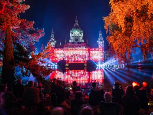 In der Ferne sitzen Menschen in einem Park und betrachten das festliche beleuchtete Neue Rathaus in Hannover bei Dunkelheit.