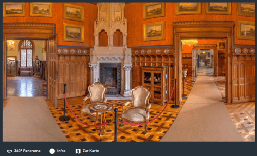 Prunkvoller Salon mit verzierten Holzvertäfelungen, Kamin, historischen Möbeln und Gemälden an den Wänden.