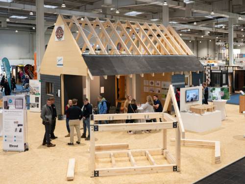 Holzbauelemente und ein Holzhaus mit offenem Dach in einer Messehalle.