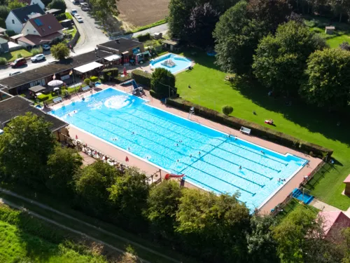 Flygfoto över utomhusbadet med simbassäng, barnbassäng, byggnader och solterrass
