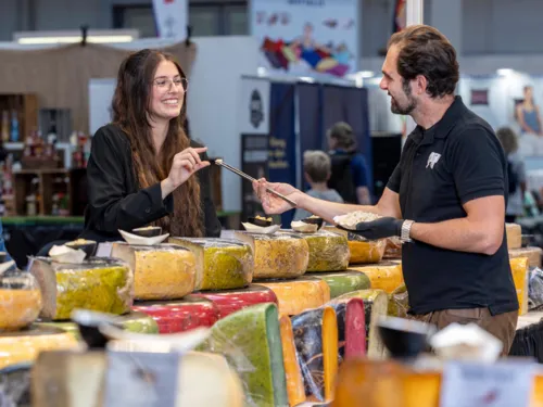 Una mujer recibe una degustación de queso de un vendedor en un puesto de quesos de la feria de experiencias y compras infa.
