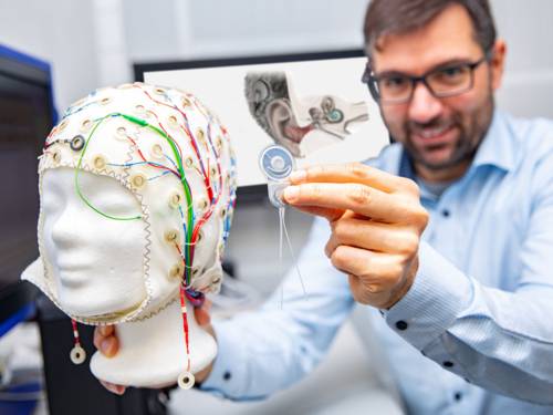 Mann hält Kopf aus Kunststoff, auf dem sich eine EEG-Haube befindet, in der Hand.