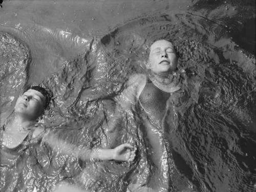 Zu sehen ist eine Schwarz-Weiß-Fotografie von zwei schwimmenden Kindern von oben.