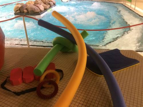Pool noodles, swimming belts, diving rings, swimming board on tiled floor at the edge of a swimming pool