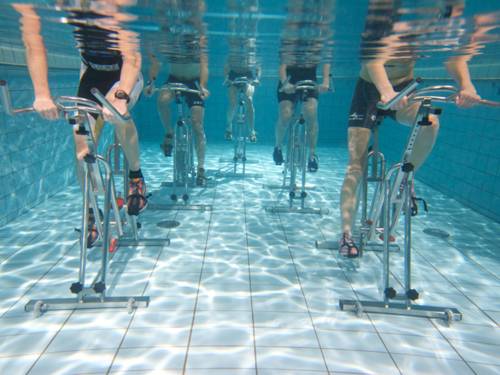 Spezielle Fahrräder im Schwimmbecken auf dem Boden stehend, Personen die darauf im Wasser radfahren