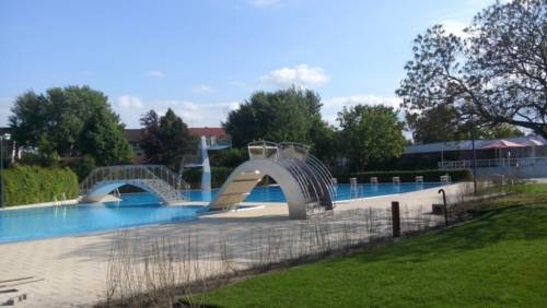 Das mit Wasser gefüllte Aussenbecken des Hallenfreibades Burgdorf ohne Badegäste bei schönem Wetter mit breiter Spaßrutsche, Sprungturm und Brücke
