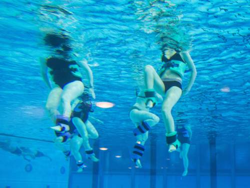 Unterwasseraufnahme von Menschen beim Aqufitnes mit Gewichtsmanschetten und Schwimmgürteln