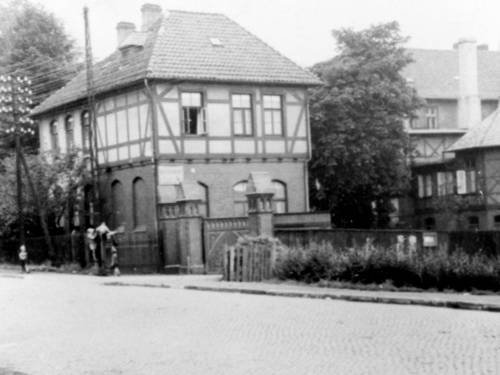 Schwarz-Weiß-Foto: Hinter einem gemauerten Eingangstor steht ein Ensemble mehrerer mehrgeschossiger Fachwerkhäuser.