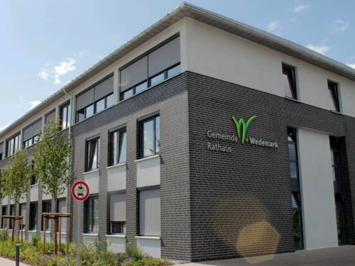 A modern building with a sloped roof; on the side is the inscription "Gemeinde Wedemark Rathaus" with a stylized green "W"