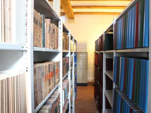 Zwei Regalreihen mit Büchern und Ordner und dazwischen ein Durchgang.