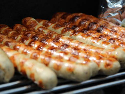 Omkring ti grillpølser på en rist, som næsten er klar til at spise.