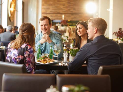 Fyra unga vuxna sitter på en elegant restaurang och pratar och njuter av en måltid med levande ljus.