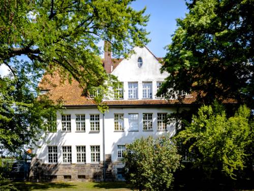 Ein zweigeschossiges, weiß angestrichenes Altbaugebäude mit vielen Fenstern und einem ausgebauten Dachgiebel.