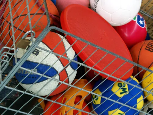 Um cesto de metal com um frisbee e várias bolas, incluindo bolas de basquetebol e de futebol