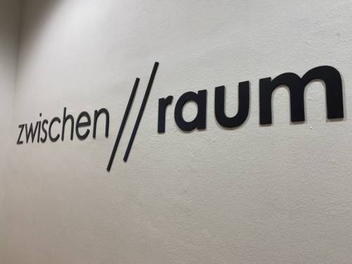 Schriftzug an einer Wand, auf dem "zwischen//raum" steht. 