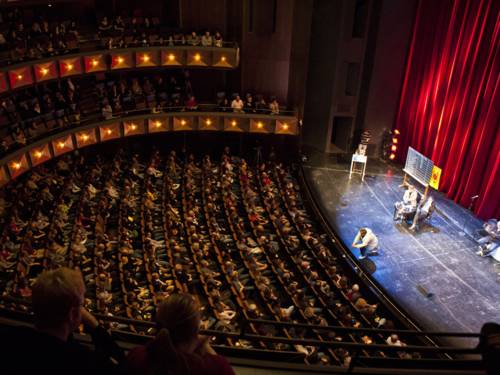 Blick von einem oberen Rang im Opernhaus auf Zuschauerraum und Bühne während einer Veranstaltung.