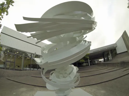 Sculpture en acier blanc avec des éléments en forme de spirale devant un bâtiment.