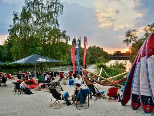 Menschen sitzen in Strandliegen an einem Fluss mit Blick auf ein Brücke