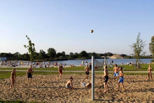 vorne Beachvolleyball spielende Jugendliche, eine Liegewiese, im Hintergrund der See