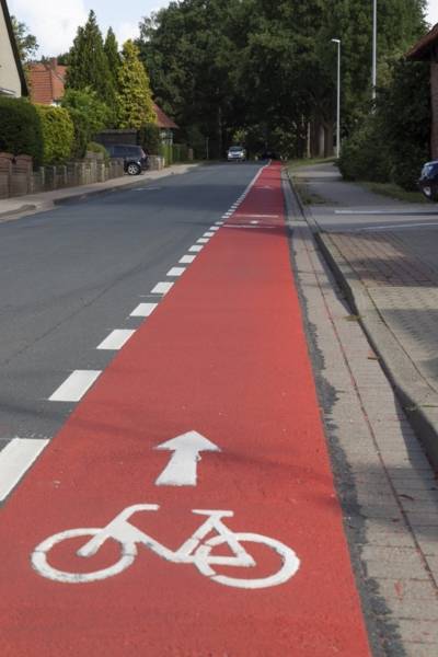 Ein roter Streifen am Rand einer Straße mit einem aufgemalten Fahrrad und einer gestrichelten weißen Linie an der Seite