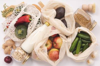 Netze voller Obst und Gemüse, dazwischen eine Milchflasche. Außerdem zwei Schraubgläser mit Reis und Haferflocken. 