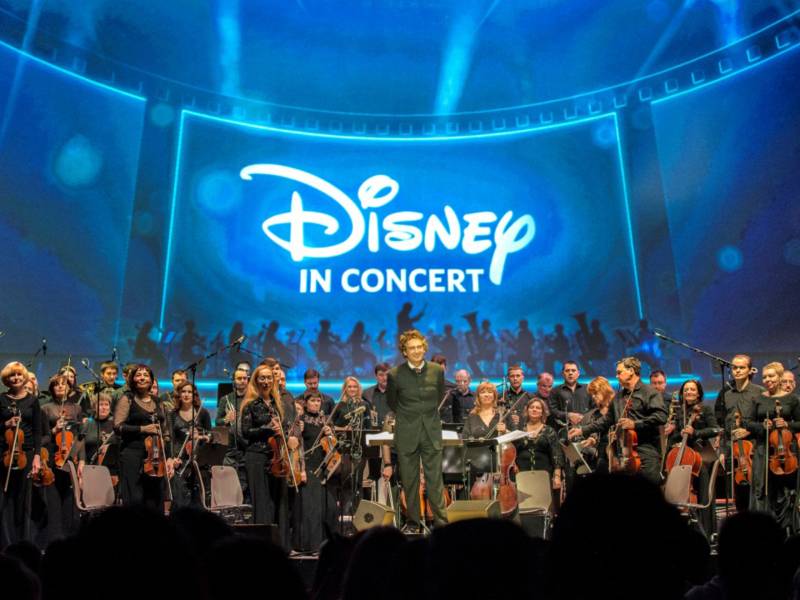 An orchestra and its conductor on a stage in front of with a large screen