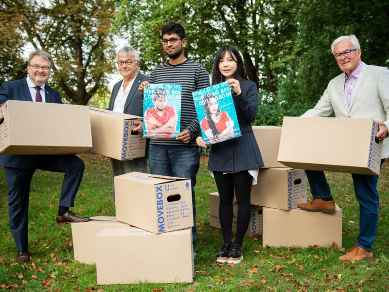 Vier Männer und eine Frau halten Plakate und Umzugskartons in den Händen