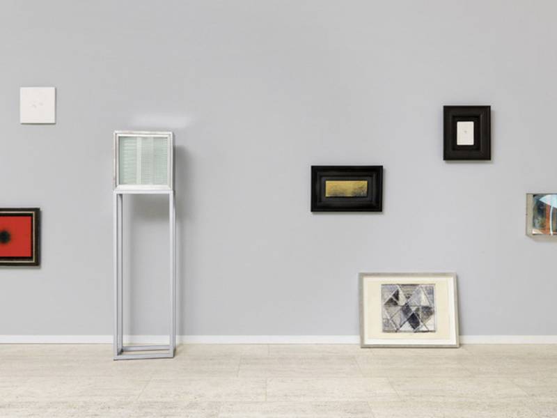 Gerahmte Bilder in verschiedenen Größen und unterschiedlichen Aufhängehöhen an einer Wand.