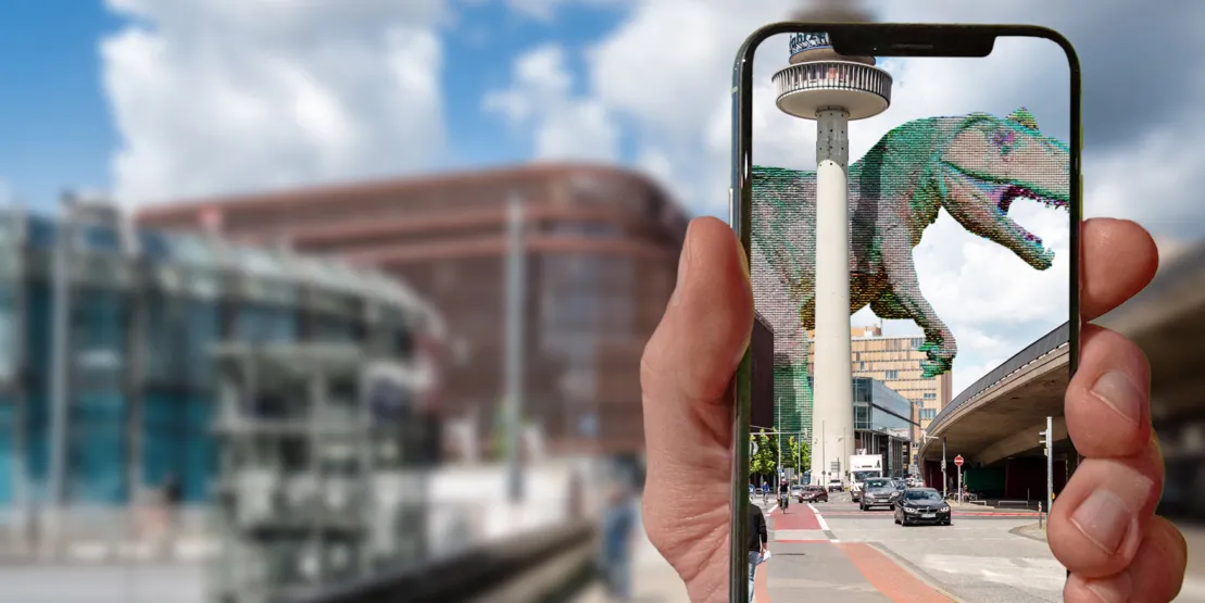 Eine Straße in Hannover. Davor hält eine Hand ein Handy. Über den Monitor wird ein Dino in die Straße eingeblendet.