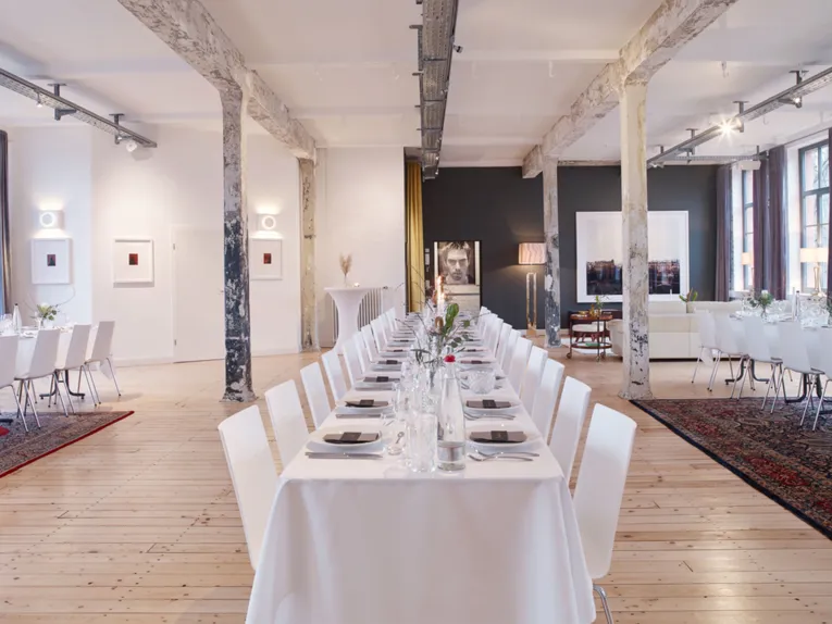 Stylish event location "Helmkehof" with long, festively laid tables, rustic pillars and modern art on the walls.