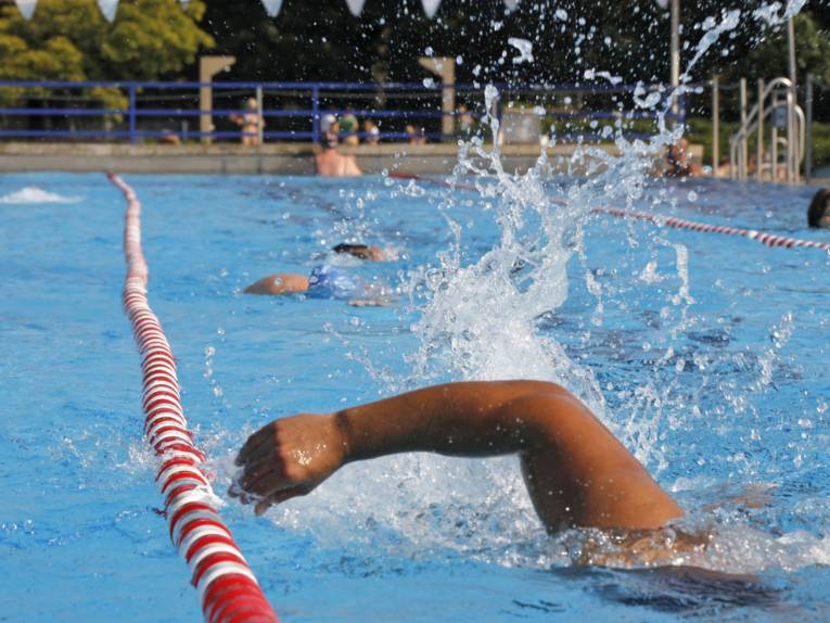 Ein Schwimmer in einem Freibad, der rechte Arm ist gerade über dem Wasser