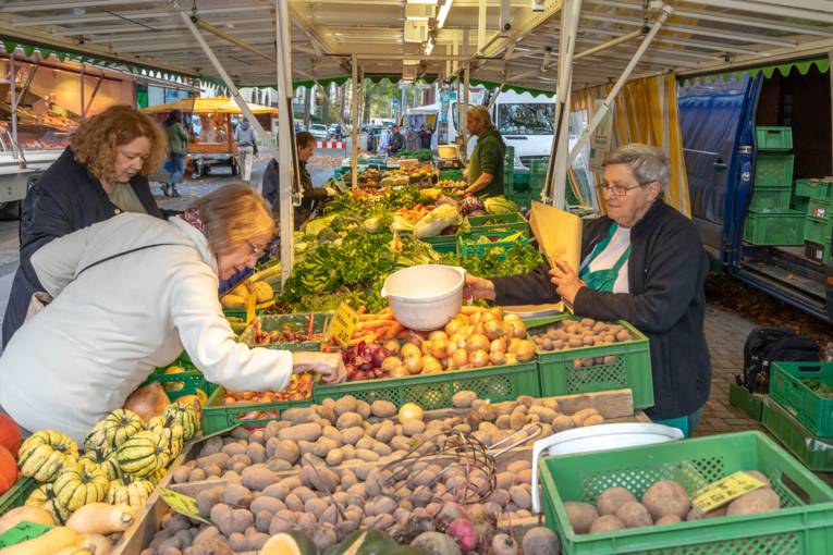 Kundinnen begutachten die Waren an einem Gem&uuml;setand auf dem Wochenmarkt.