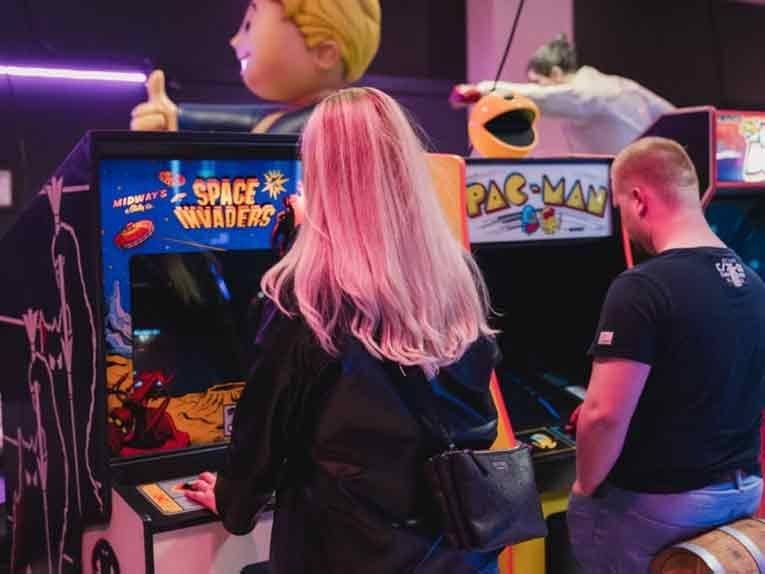 Eine Frau und ein Mann spielen jeweils an einem Videospielautomat